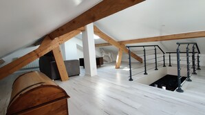 Een zolderkamer met zichtbare houten balken, een hoogslaper, een kleine trap en een houten kist.