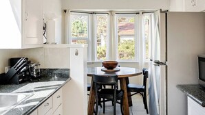 Eine moderne Küche mit weißen Schränken, einer Arbeitsplatte aus Granit, einem Esstisch mit Stühlen und einem Kühlschrank.