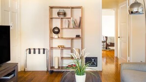 Ein Wohnzimmer mit einer Holzbibliothek, einem TV-Schrank, einer Topfpflanze und einem Durchgang zu einem anderen Raum.