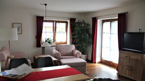 Una sala de estar con una mesa de comedor, sillas, un sofá, un televisor y una planta grande.