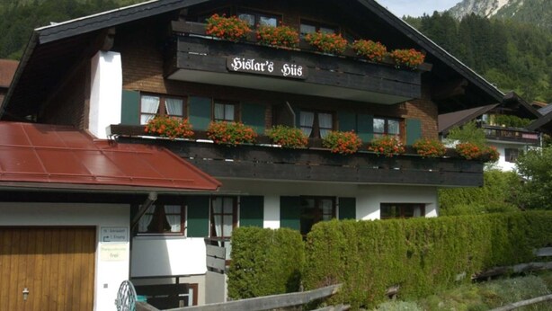 Un edificio de madera tradicional con un letrero que dice "Sister's Haus" y jardineras con flores en el nivel superior.