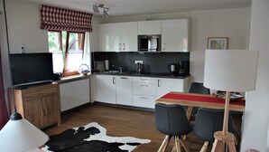 Una cocina moderna con armarios blancos, encimera negra y un comedor con mantel rojo.