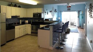 A kitchen with white cabinets, a microwave, a stove, and a bar area with stools. - Gulf View Condo, Sleeps 6, Pool, Steps to Beach (Madeira Beach)
