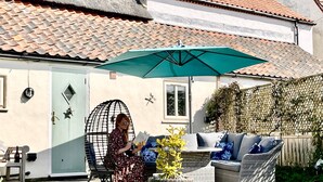 Eine Terrasse mit Gartenmöbeln, einem grünen Sonnenschirm und einem Haus mit Ziegeldach.