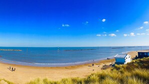 Ein Strand mit blauem Himmel, sandigem Ufer und einem Leuchtturm in der Ferne.