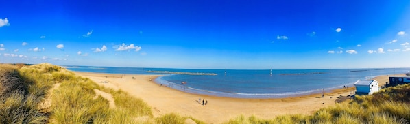 A beach with a clear sky, sandy shore, and a lighthouse in the distance.