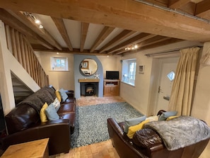 A cozy living room with a fireplace, wooden beams, a sofa, and a television.