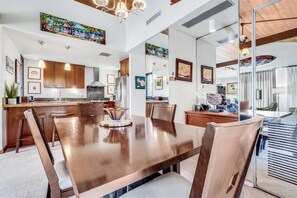A modern kitchen with wooden cabinets, a large dining table, and pendant lighting.