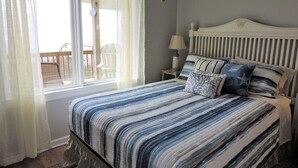 A bedroom with a bed, a nightstand, a lamp, and a view of the outdoors. - Bright 3BR Beach Home with Deck & Ocean Views (Emerald Isle)