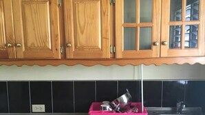 A kitchen with wooden cabinets, a pink dish rack, and black tiled backsplash. - Froggy’s Guest House (Westmoreland)