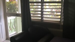 A room with a bed, a chair, a window with blinds, and a view of greenery outside. - Froggy’s Guest House (Westmoreland)