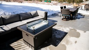 Une terrasse avec une table basse en verre, un canapé gris et des chaises en osier.