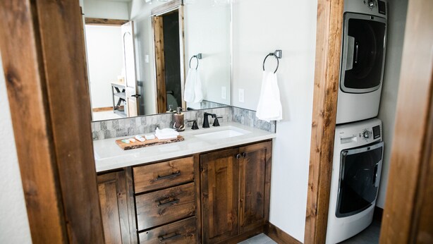 Une salle de bain moderne avec un meuble-lavabo en bois, un grand miroir, un évier et une laveuse et une sécheuse superposées.