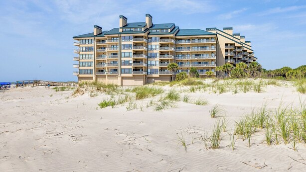 Ett hotell med flera våningar och balkonger, beläget på en sandstrand med vegetation i förgrunden.