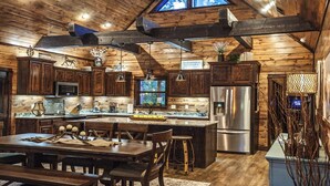 A rustic kitchen with wooden cabinets, a stainless steel refrigerator, and a large island with a sink. - Choctaw Wind: Luxurious, Outdoor Furniture, Shuffleboard, Large Hot Tub🛋️🛁🔥 (Broken Bow)