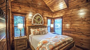 A wooden cabin bedroom with a bed, nightstands, and a decorative window. - Choctaw Wind: Luxurious, Outdoor Furniture, Shuffleboard, Large Hot Tub🛋️🛁🔥 (Broken Bow)