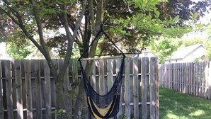 Eine Hängematte, die an einem Baum im Garten zwischen einem Holzzaun befestigt ist.