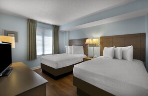 Une chambre d’hôtel avec deux lits, un bureau avec un ordinateur et une fenêtre avec des rideaux.