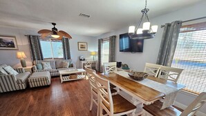 Ein geräumiges Wohnzimmer mit einem Holzesstisch, weißen Stühlen und einer Sofagarnitur.