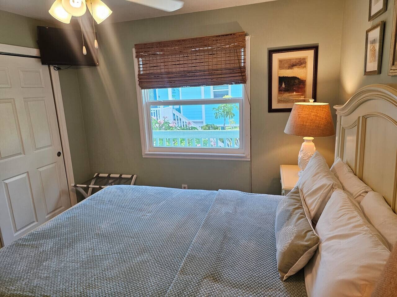 Une chambre à coucher avec un lit, une fenêtre donnant sur un beau paysage, une lampe de chevet et un ventilateur de plafond.