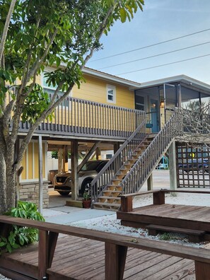 Una casa de dos pisos con un porche cubierto, una escalera y un área exterior cercada.