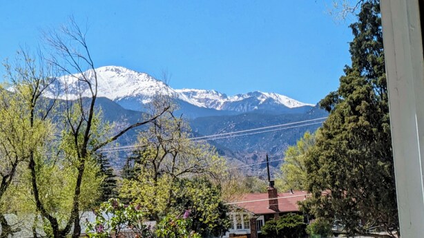 Paisaje montañoso con picos nevados, cielo azul despejado y vista de un edificio con techo rojo.