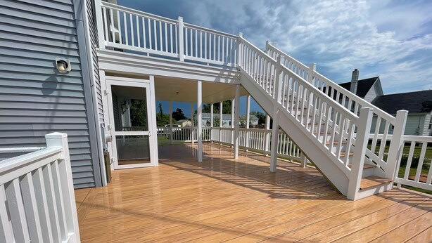 Una terraza de madera con barandas blancas y una puerta de vidrio que da a un espacio cubierto.