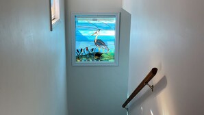 Una escalera con una obra de arte enmarcada de un pájaro, una ventana con vista al cielo y una barandilla.