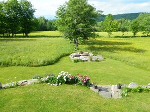 A well-maintained grassy area with a stone structure, surrounded by trees and flowers. - Classic Green Mountain Cabin (Mt Holly)