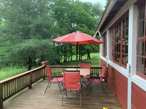A wooden deck with a table and chairs, a red umbrella, and a view of trees. - Classic Green Mountain Cabin (Mt Holly)