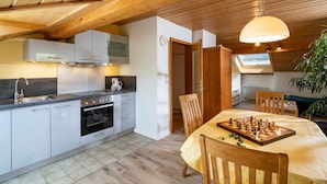 Une cuisine moderne avec des poutres en bois, un coin repas agrémenté d’un échiquier et un espace de vie chaleureux.