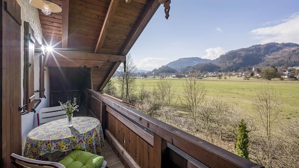 Un balcon en bois, agrémenté d’une table et de chaises, qui offre une vue sur un champ verdoyant et des collines.