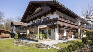 Un chalet traditionnel avec une façade en bois, de grandes fenêtres et un chemin en pierre menant à l’entrée.