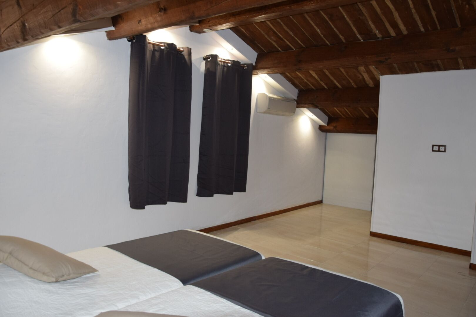 A room with a bed, two black curtains, a ceiling fan, and a light fixture.