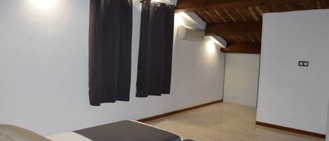 A room with a bed, two black curtains, a ceiling fan, and a light fixture.