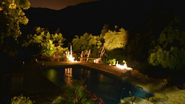 Vista nocturna de una piscina rodeada de árboles y un sendero de piedra.