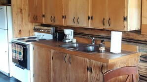 Une cuisine rustique, située dans une cabane en bois, avec un îlot central, des armoires en bois, une cuisinière et une machine à café.