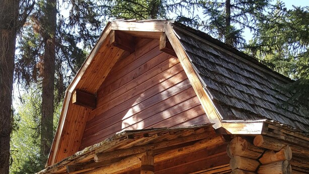 Une cabane rustique en rondins de bois, dotée d’une véranda, de bancs en bois et d’une grande fenêtre.