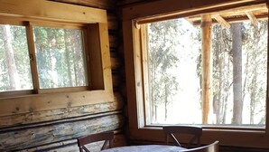 L’intérieur d’un chalet rustique en bois, avec une table et des chaises, de grandes fenêtres et un plancher en bois.