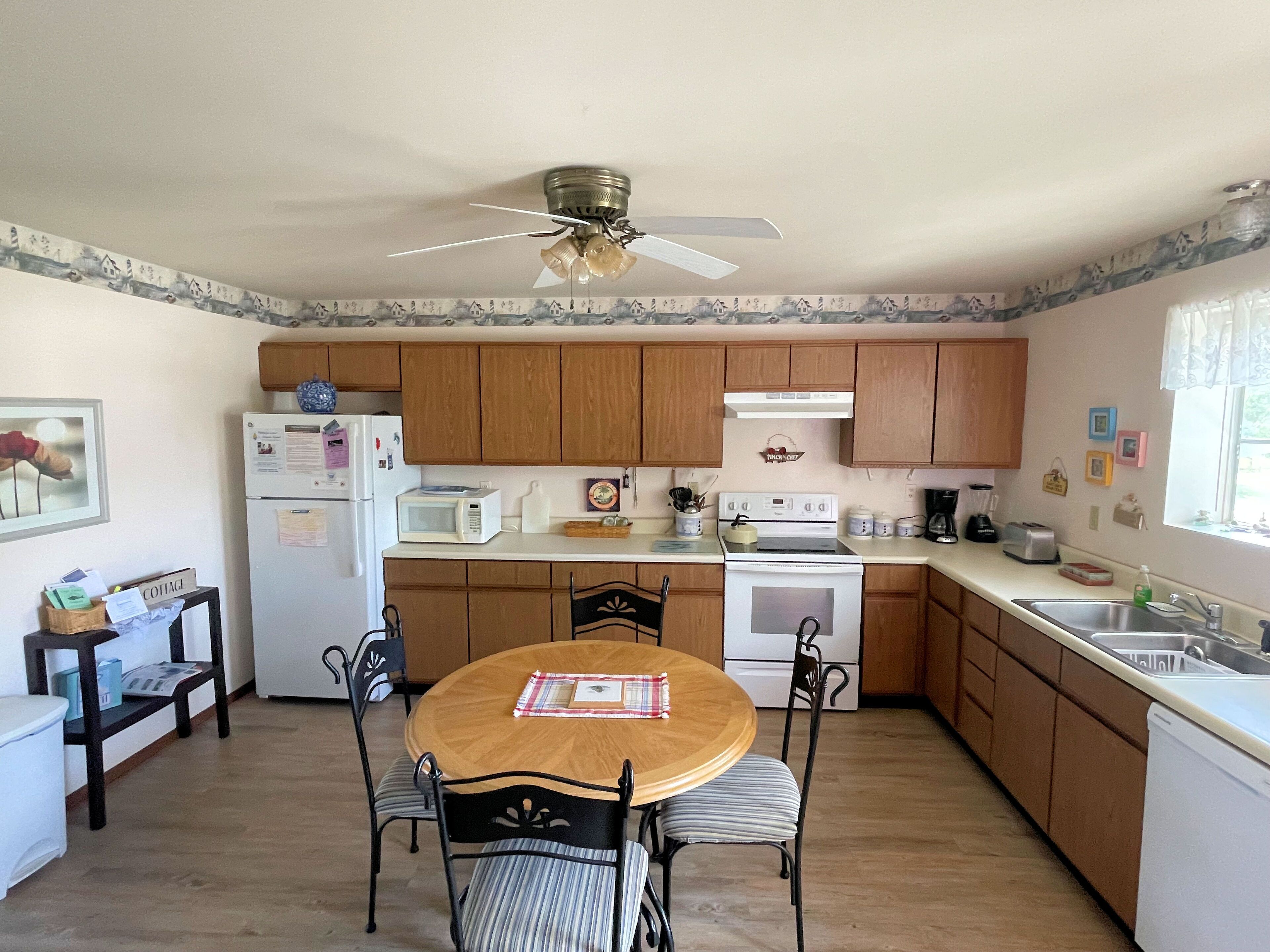 A compact kitchen with wooden cabinets, a white refrigerator, a microwave, a stove, and a ceiling fan.