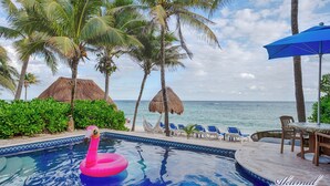 Una piscina con un flotador de flamenco rosa, rodeada de palmeras y vista a la playa.
