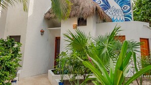 Un edificio blanco con techo de paja, rodeado de palmeras y plantas en macetas.