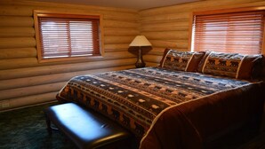 Camera da letto in una baita di legno, con un letto, una panca e due finestre con persiane.