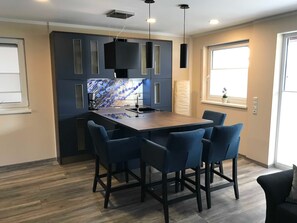 Uma cozinha moderna com uma ilha central, cadeiras azul-escuras e iluminação pendente.