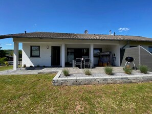 Uma casa moderna com alpendre coberto, churrasqueira e um pequeno jardim.