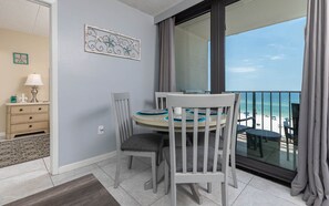 Un balcon avec vue sur la plage, une table à manger avec des chaises, un petit meuble et un élément décoratif mural.