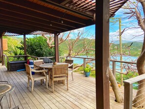 A wooden deck with a table and chairs, overlooking a body of water and greenery. - Into the Mystic Lower Suite with POOL and VIEWS! (Coral Bay)