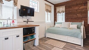 Un dormitorio con cama, televisor, pared de madera y ventana con cortinas.