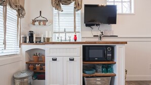 Cocina compacta con microondas integrado, cafetera y televisor sobre la encimera.