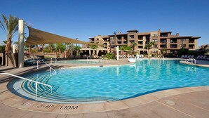 A swimming pool with a sunshade, lounge chairs, and a building with multiple balconies in the background.